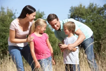 Familien(ferien)woche für die Ehe Familie(ferien)woche: glückliche familie - ehepaar mit ihren beiden kindern auf einer wiese mit bäumen