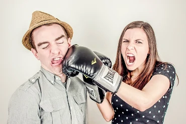 Eine Frau mit Boxhandschuhen steht neben einem Mann und boxt ihm ins Gesicht