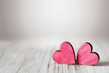 Zwei beieinander liegende rosa Herzen auf grauem hölzernem Hintergrund