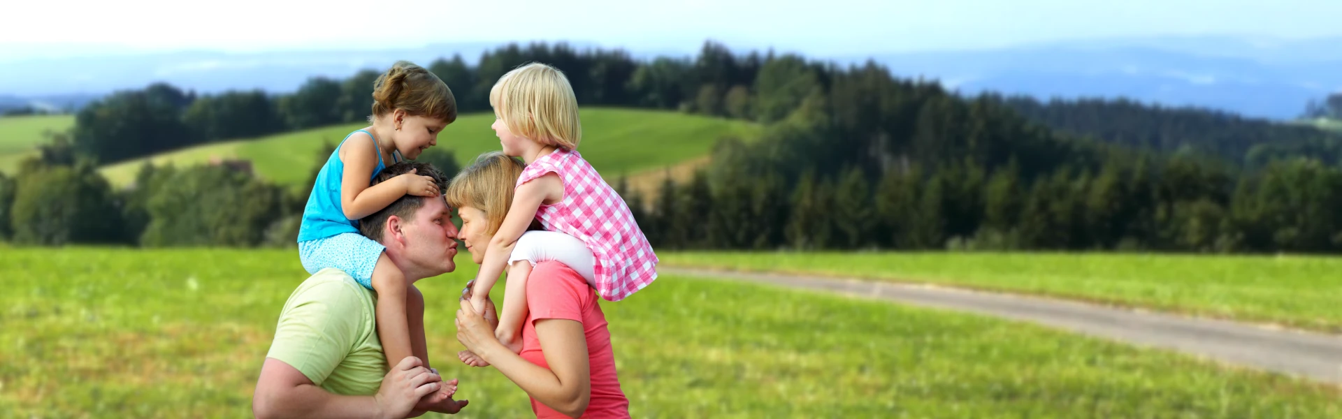 Glückliches Ehepaar mit Kindern auf den Schultern küsst sich bei einer Wanderung im Schwarzwald – Familienwoche mit Kinderbetreuung.