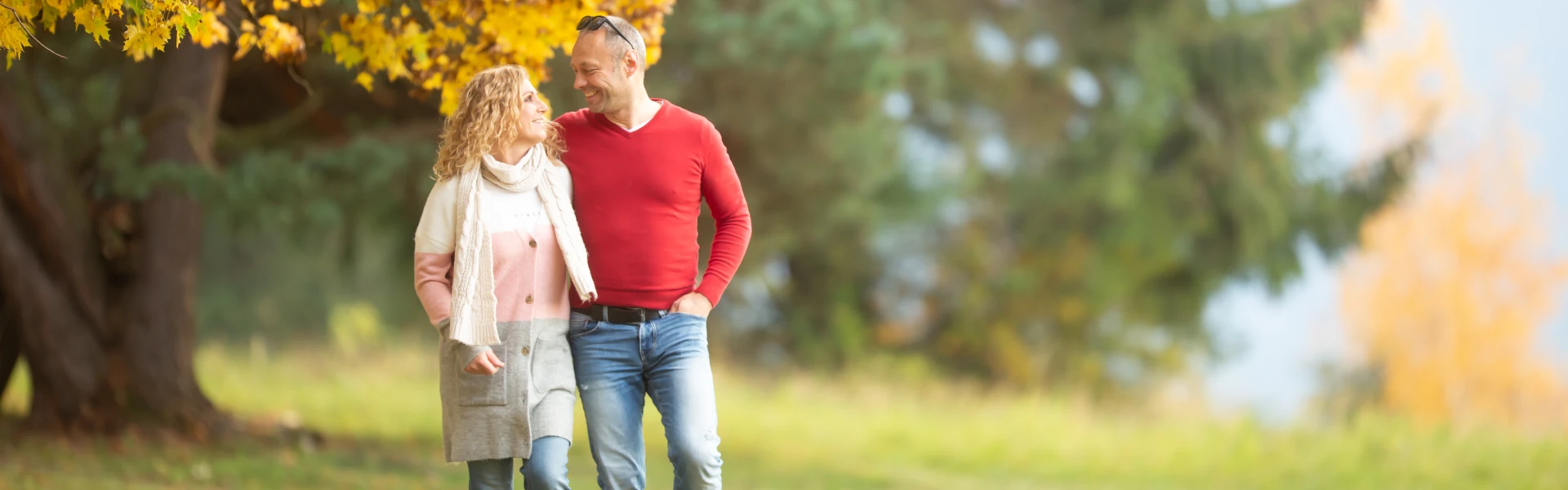 Ein engumschlungenes Ehepaar spaziert durch den Park und schaut sich lächelnd an – Titelbild des Ehepaarkurses zur Paarkommunikation.