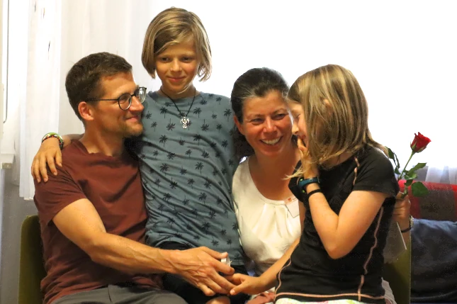 Vater, Mutter und zwei Kinder sitzen gllücklich umarmend auf dem Sofa währrend der Familienwoche in Schramberg