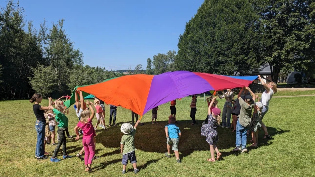 Kinder mit Betreuerinnen beim Fallschirm-Schwungtuchspiel