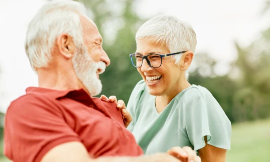 aelteres Paar schaut sich in einem Park sitzend gluecklich an