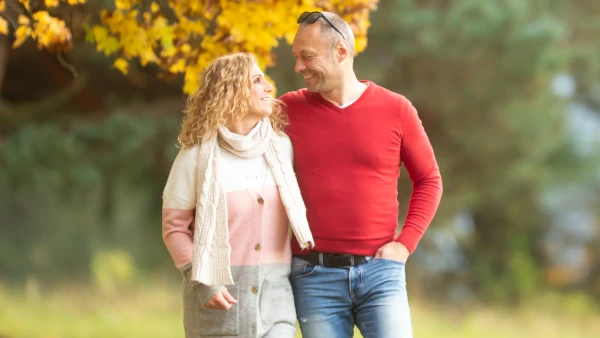 Ein Ehepaar geht engumschlungen durch den Park und blickt sich lächelnd an - Ehepaarkus