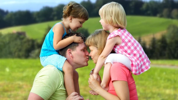 Glückliches Ehepaar mit Kindern auf den Schultern küsst sich bei einer Wanderung im Schwarzwald – Familienwoche mit Kinderbetreuung.